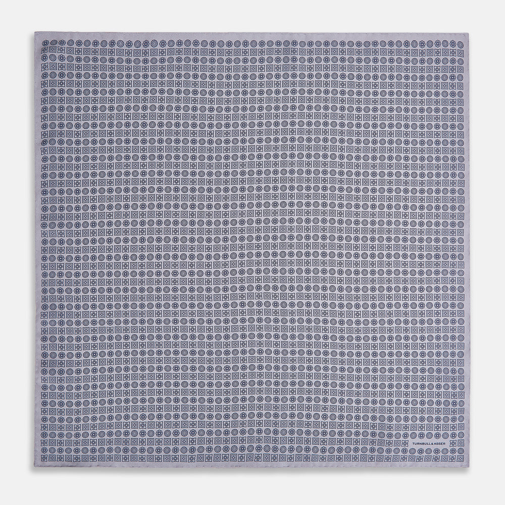 A lilac silk pocket square featuring a repeating geometric rosette pattern. One corner is folded over to show the reverse side, and "Turnbull & Asser UK" is printed in the bottom right corner.