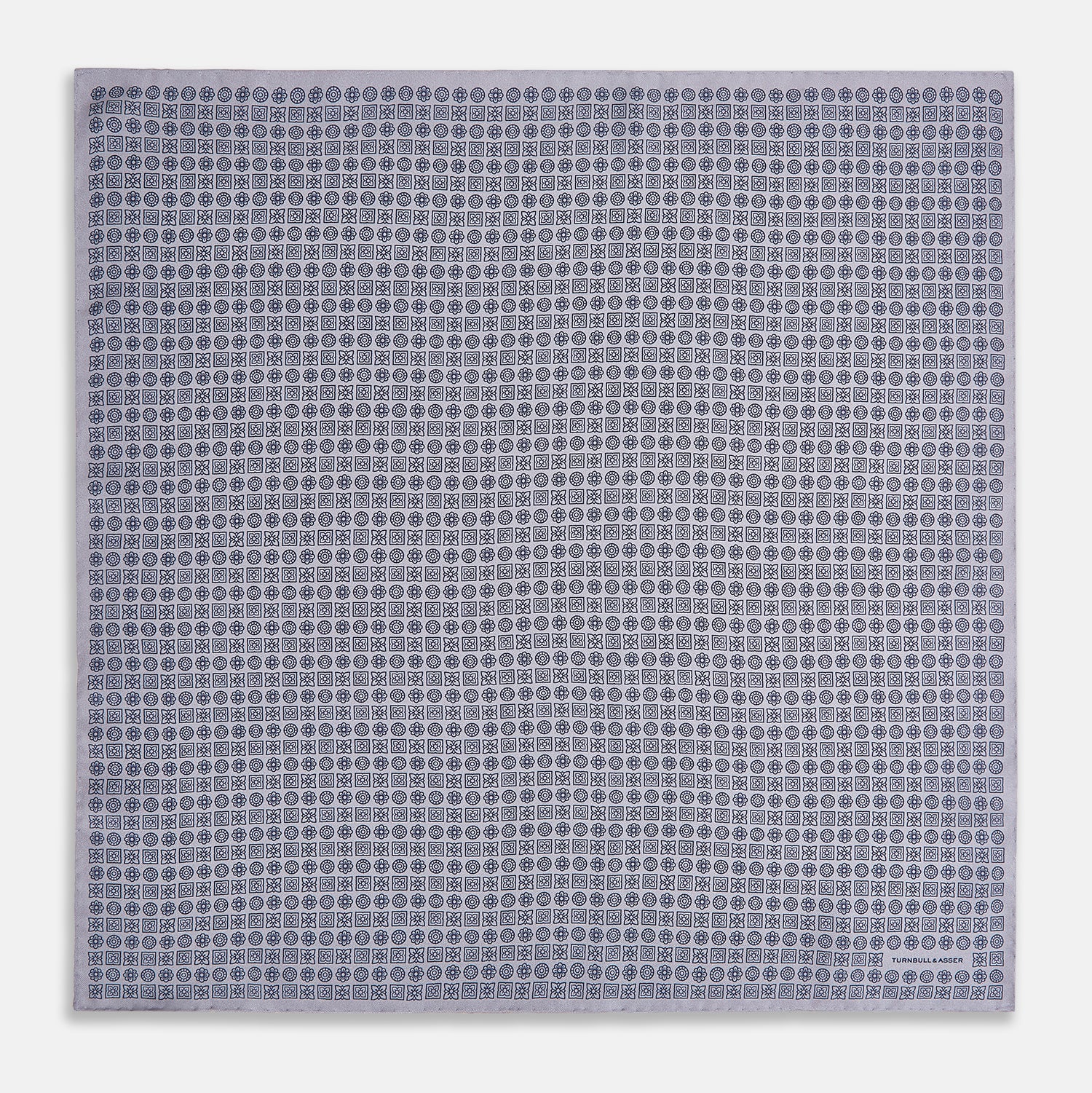 View 4 of product A lilac silk pocket square featuring a repeating geometric rosette pattern. One corner is folded over to show the reverse side, and "Turnbull & Asser UK" is printed in the bottom right corner.