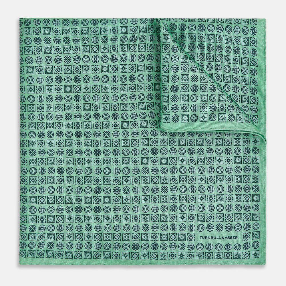 Floral Green Pocket Square in Silk by Turnbull & Asser UK, showcasing navy-blue floral geometric motifs on a bright green background. One corner is neatly folded to display both sides of the silk fabric, with "Turnbull & Asser UK" printed in the lower right corner.