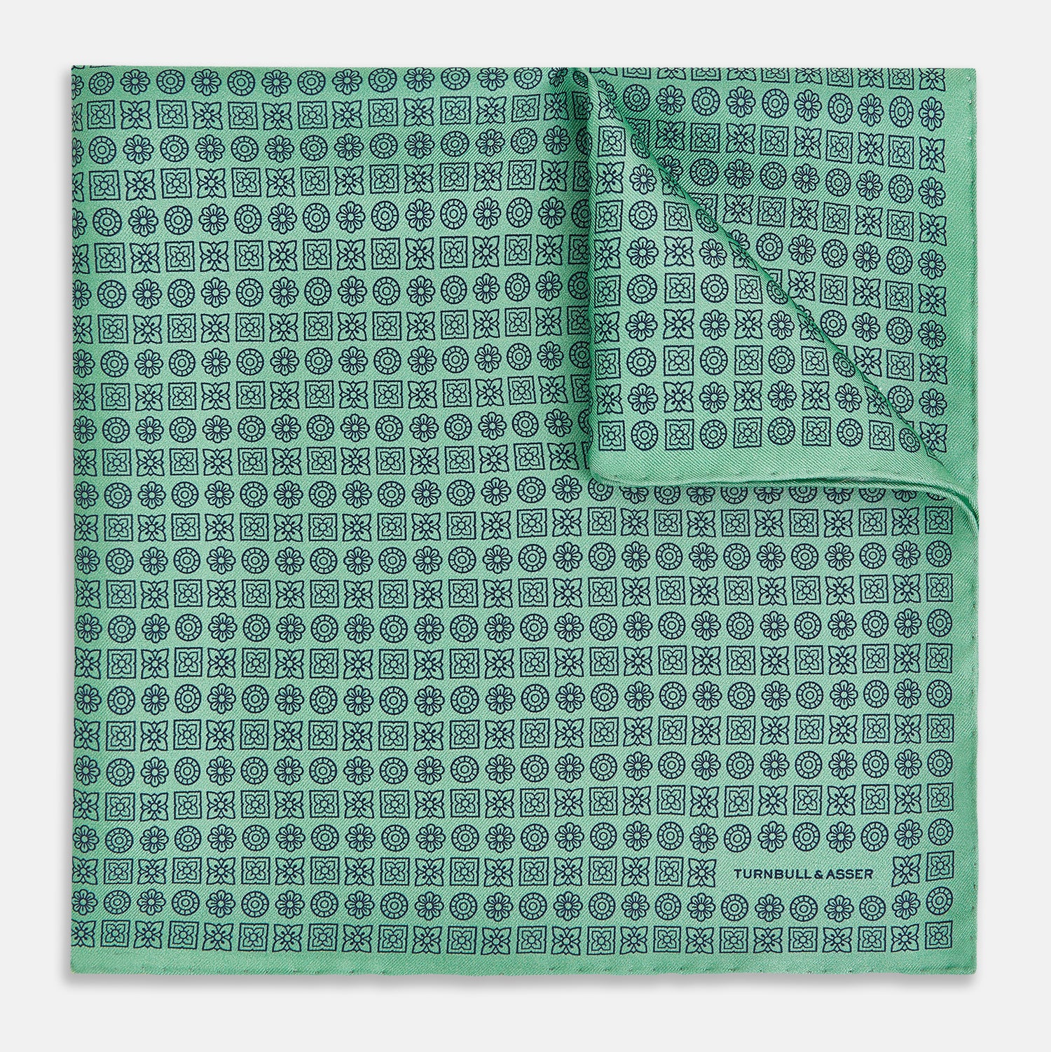 View 1 of product Floral Green Pocket Square in Silk by Turnbull & Asser UK, showcasing navy-blue floral geometric motifs on a bright green background. One corner is neatly folded to display both sides of the silk fabric, with "Turnbull & Asser UK" printed in the lower right corner.