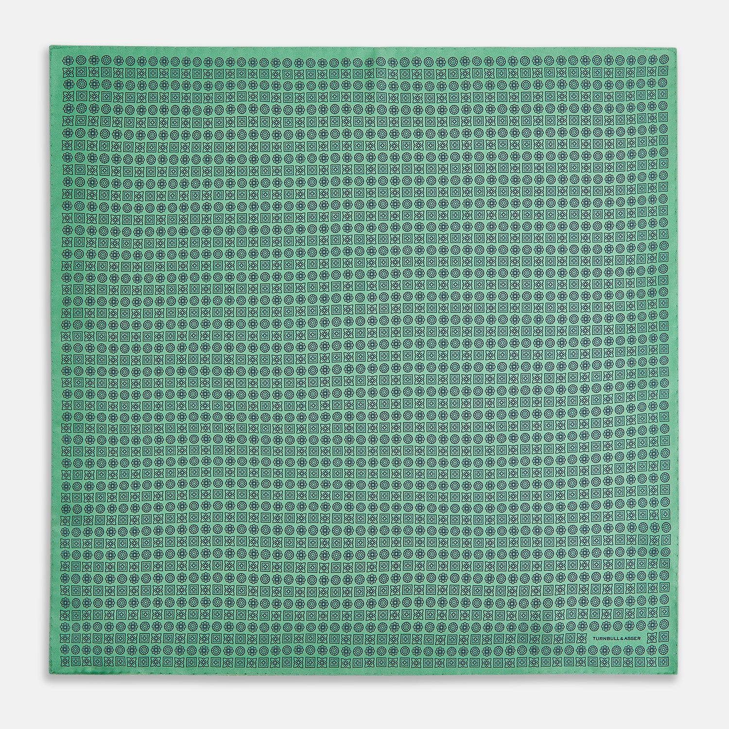 View 4 of product Floral Green Pocket Square in Silk by Turnbull & Asser UK, showcasing navy-blue floral geometric motifs on a bright green background. One corner is neatly folded to display both sides of the silk fabric, with "Turnbull & Asser UK" printed in the lower right corner.