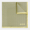 View 1 of product A Floral Yellow Pocket Square in Silk by Turnbull & Asser UK, showcasing a repeating black geometric pattern with subtle floral motifs and the brand logo in one corner. One corner of the fabric is folded over to display the reverse side.