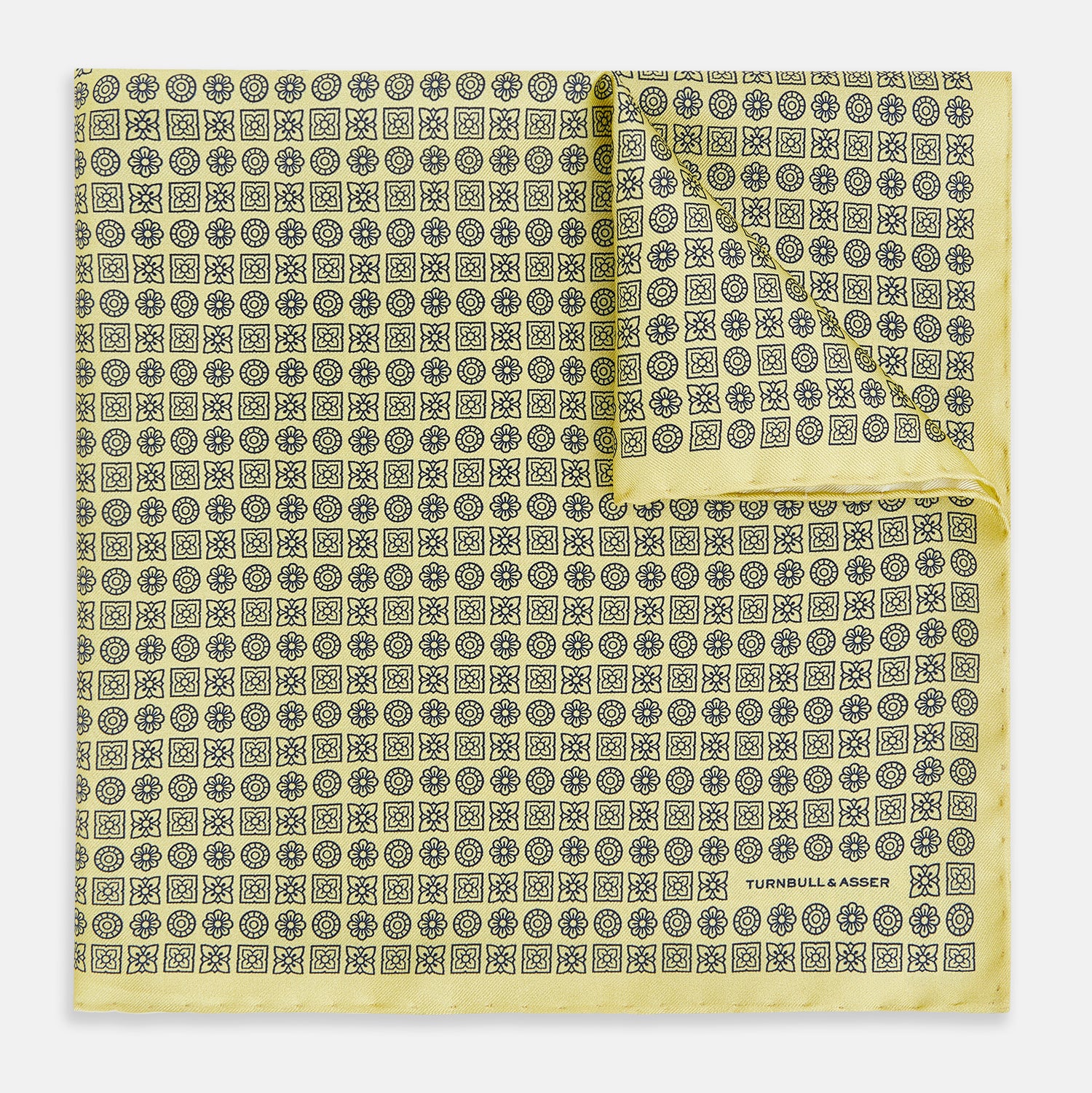 View 1 of product A Floral Yellow Pocket Square in Silk by Turnbull & Asser UK, showcasing a repeating black geometric pattern with subtle floral motifs and the brand logo in one corner. One corner of the fabric is folded over to display the reverse side.