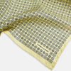 View 2 of product A Floral Yellow Pocket Square in Silk by Turnbull & Asser UK, showcasing a repeating black geometric pattern with subtle floral motifs and the brand logo in one corner. One corner of the fabric is folded over to display the reverse side.