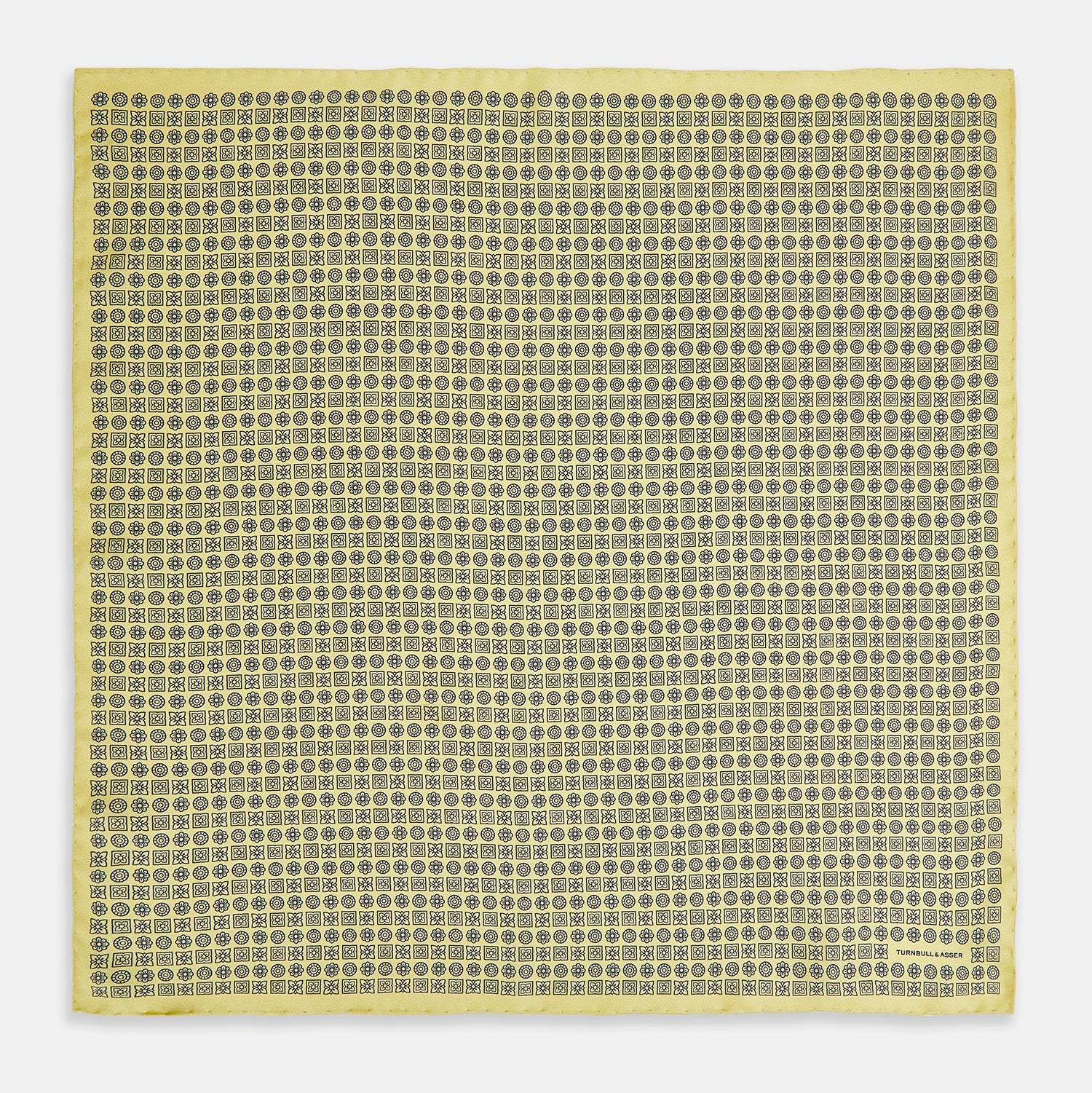 View 4 of product A Floral Yellow Pocket Square in Silk by Turnbull & Asser UK, showcasing a repeating black geometric pattern with subtle floral motifs and the brand logo in one corner. One corner of the fabric is folded over to display the reverse side.