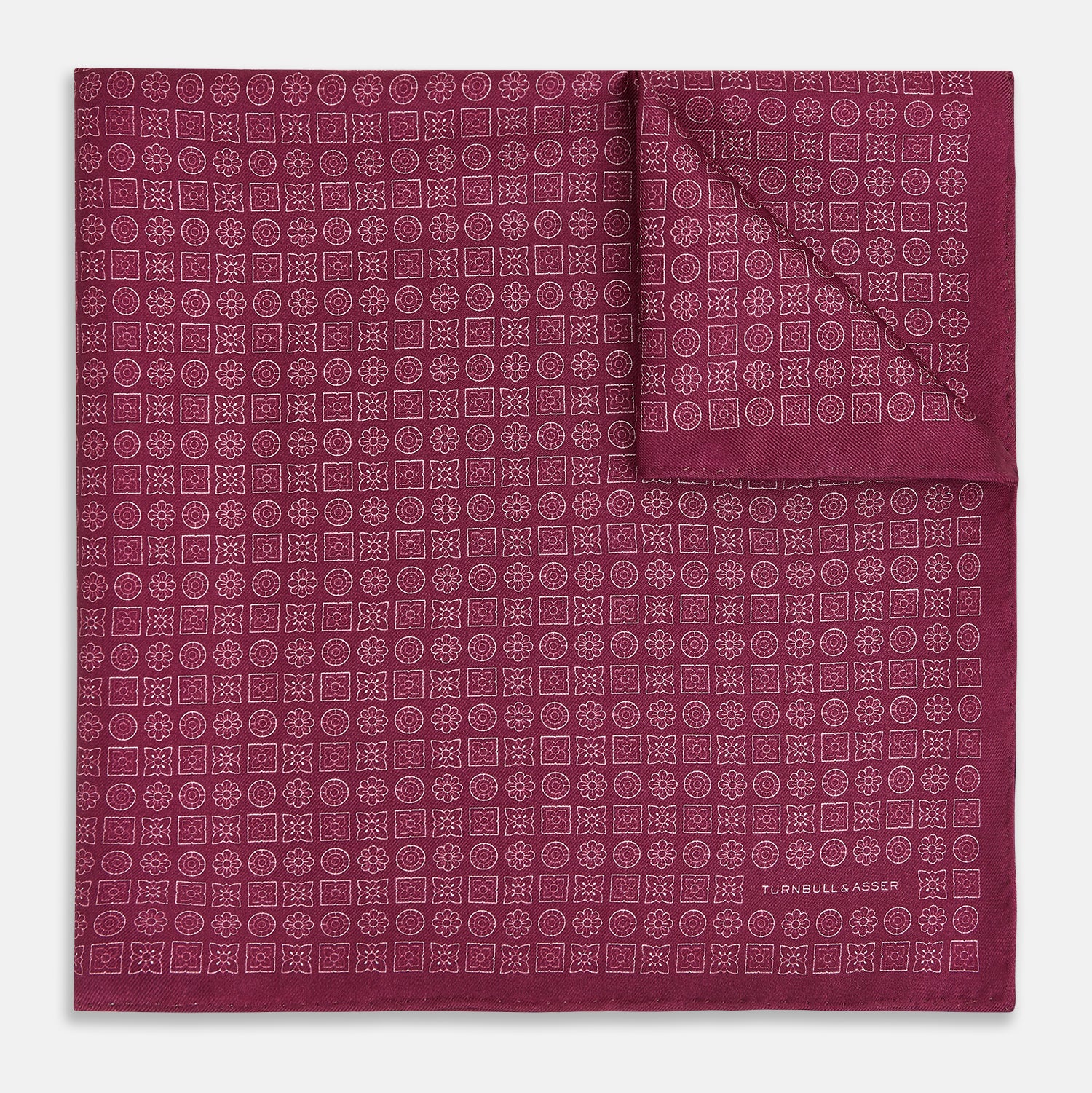 View 1 of product A folded Floral Burgundy Pocket Square in Silk by Turnbull & Asser UK, adorned with pink floral geometric motifs and featuring the Turnbull & Asser logo in the bottom right corner.