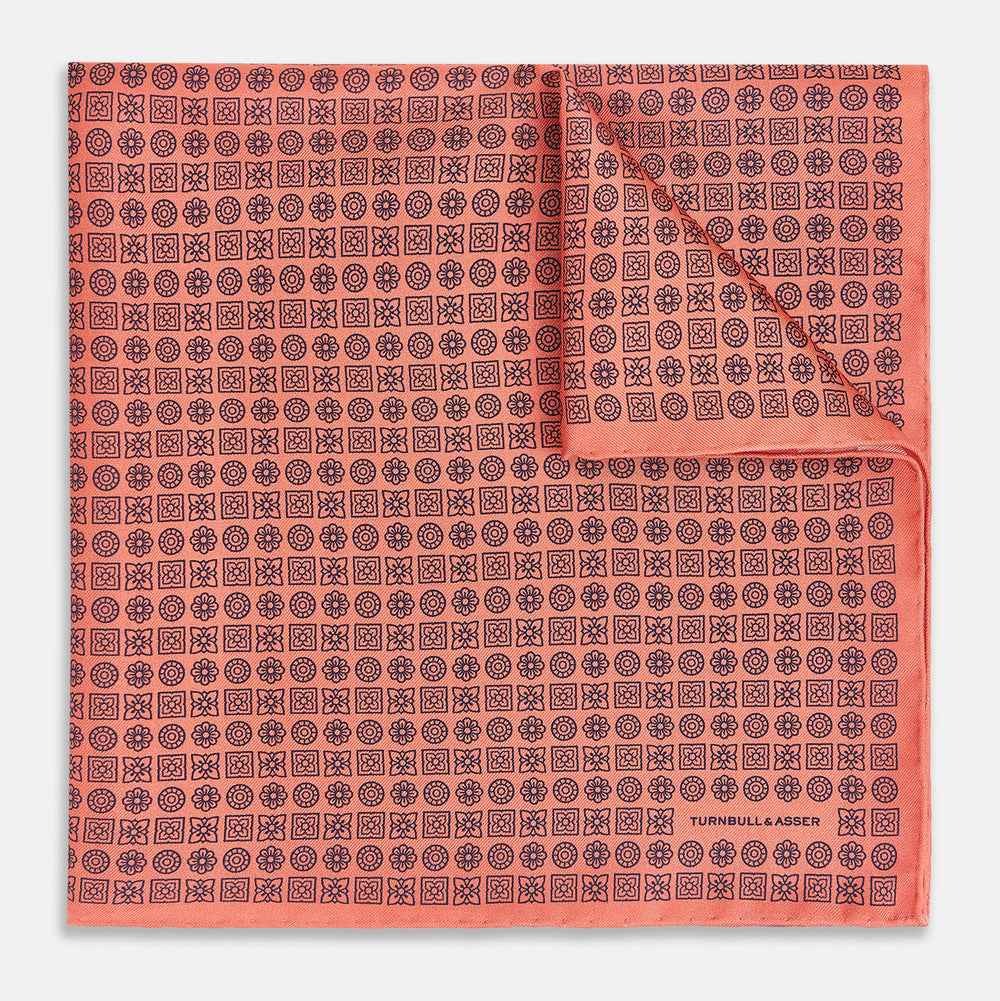 The Floral Orange Pocket Square in Silk by Turnbull & Asser UK features a coral and navy geometric floral pattern with orange accents, neatly folded at the corner. The brand name, Turnbull & Asser UK, is printed in white near the edge.