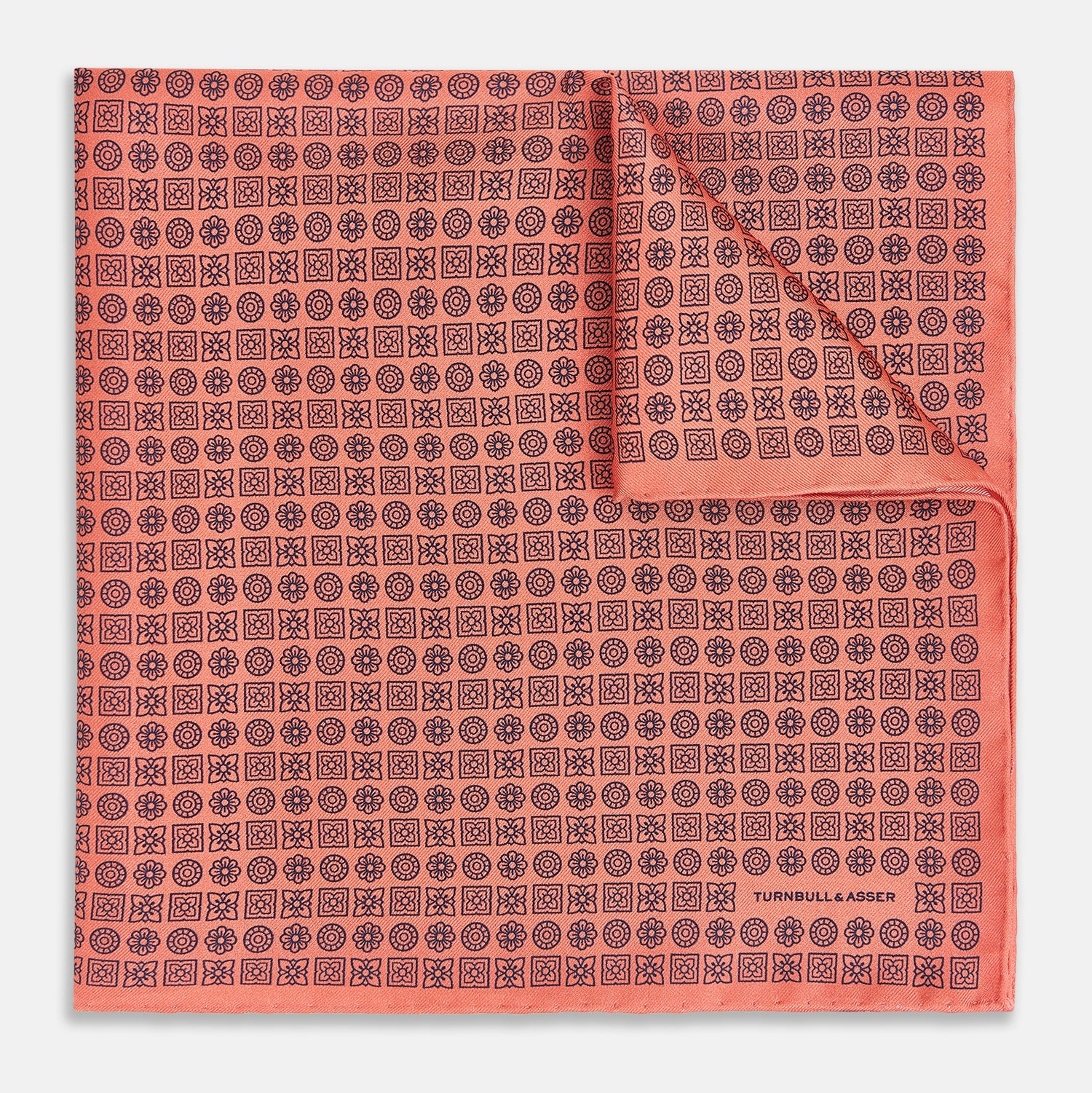 View 1 of product The Floral Orange Pocket Square in Silk by Turnbull & Asser UK features a coral and navy geometric floral pattern with orange accents, neatly folded at the corner. The brand name, Turnbull & Asser UK, is printed in white near the edge.