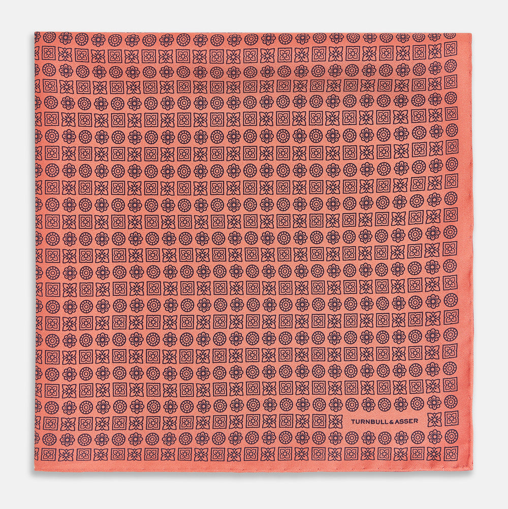 The Floral Orange Pocket Square in Silk by Turnbull & Asser UK features a coral and navy geometric floral pattern with orange accents, neatly folded at the corner. The brand name, Turnbull & Asser UK, is printed in white near the edge.