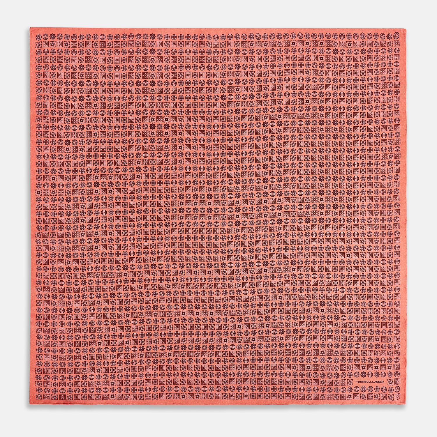 View 4 of product The Floral Orange Pocket Square in Silk by Turnbull & Asser UK features a coral and navy geometric floral pattern with orange accents, neatly folded at the corner. The brand name, Turnbull & Asser UK, is printed in white near the edge.