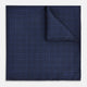 The Checked Blue On Navy Pocket Square in Silk by Turnbull & Asser UK is crafted from dark blue silk and features a subtle geometric design with a lighter blue grid pattern, finished with a discreet Turnbull & Asser logo in the corner.