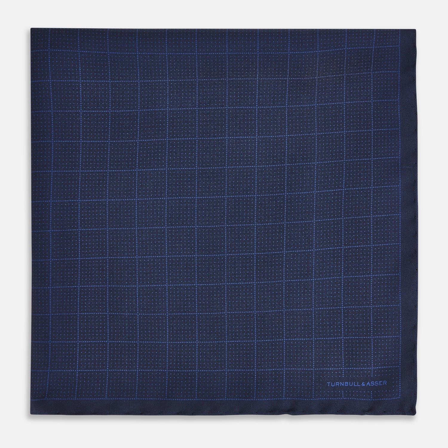 View 3 of product The Checked Blue On Navy Pocket Square in Silk by Turnbull & Asser UK is crafted from dark blue silk and features a subtle geometric design with a lighter blue grid pattern, finished with a discreet Turnbull & Asser logo in the corner.