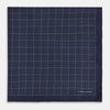 View 3 of product Checked Navy On White Pocket Square in Silk by Turnbull & Asser UK, featuring a navy blue geometric pattern with a white dotted grid and a solid border. The pocket square is shown with one corner folded over to display the “TURNBULL & ASSER” label in white text.