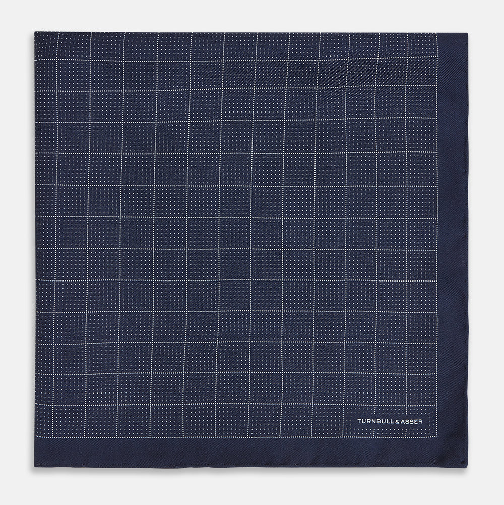 Checked Navy On White Pocket Square in Silk by Turnbull & Asser UK, featuring a navy blue geometric pattern with a white dotted grid and a solid border. The pocket square is shown with one corner folded over to display the “TURNBULL & ASSER” label in white text.