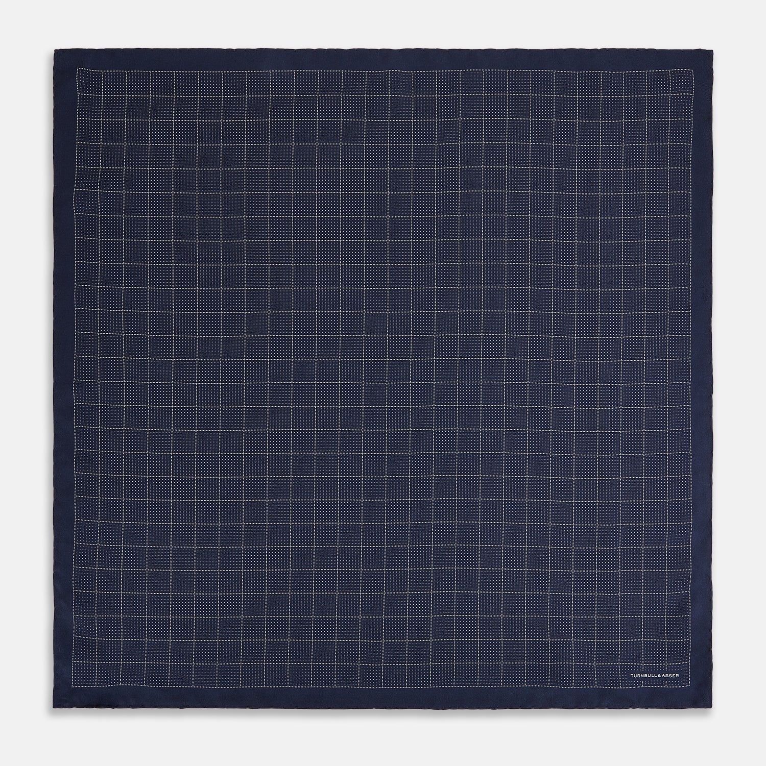 View 4 of product Checked Navy On White Pocket Square in Silk by Turnbull & Asser UK, featuring a navy blue geometric pattern with a white dotted grid and a solid border. The pocket square is shown with one corner folded over to display the “TURNBULL & ASSER” label in white text.