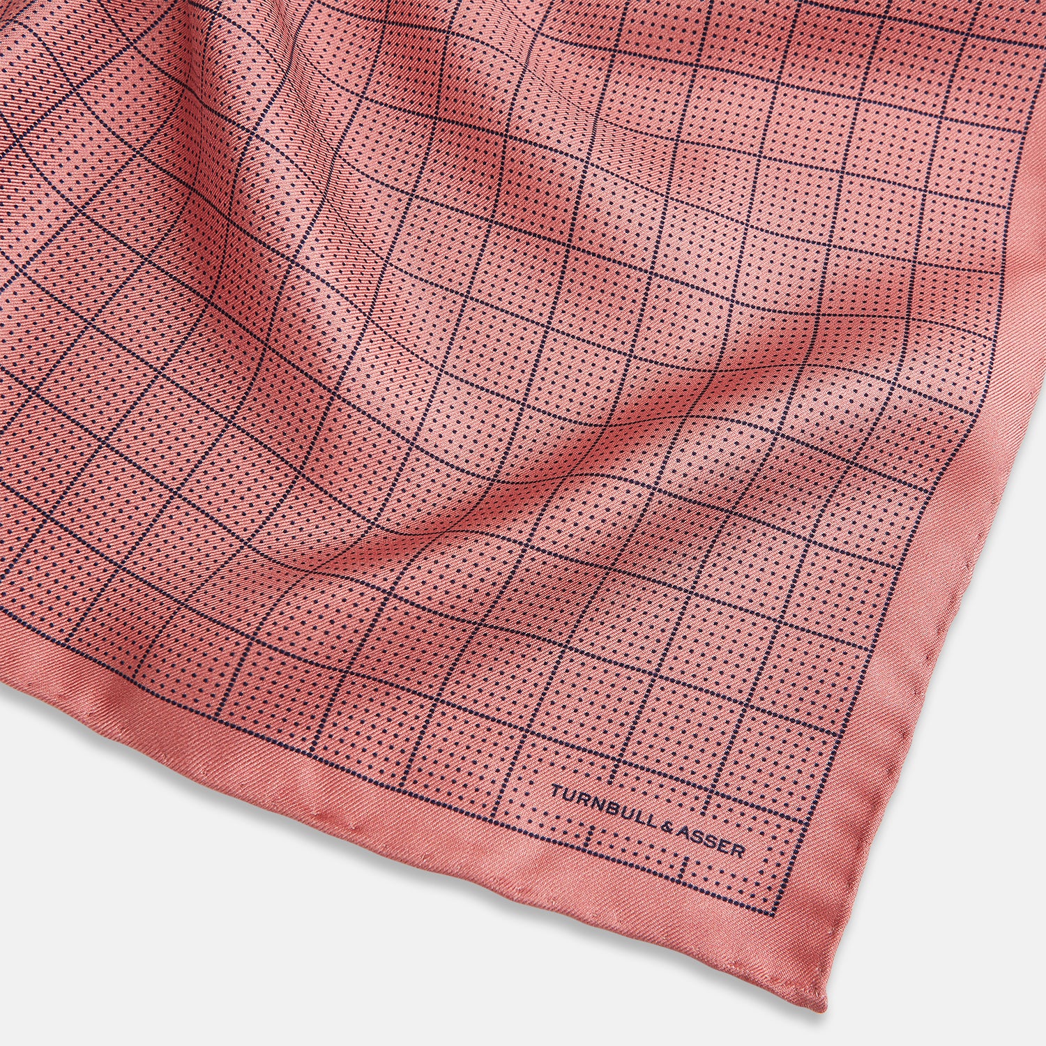 View 2 of product Introducing the Checked Pink Pocket Square in Silk from Turnbull & Asser UK, crafted with a geometric grid pattern of black lines and micro dots on soft pink silk. The design features a neatly folded corner and "Turnbull & Asser" subtly printed in the bottom right.
