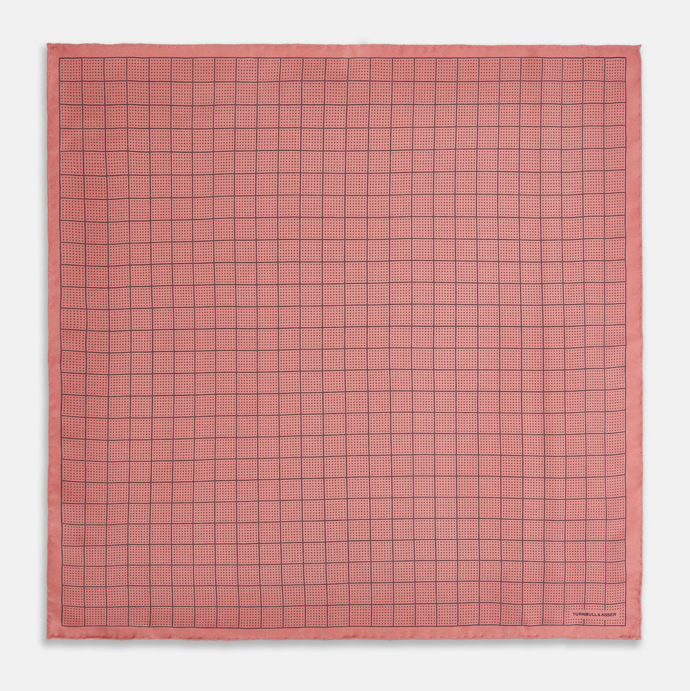 Introducing the Checked Pink Pocket Square in Silk from Turnbull & Asser UK, crafted with a geometric grid pattern of black lines and micro dots on soft pink silk. The design features a neatly folded corner and "Turnbull & Asser" subtly printed in the bottom right.