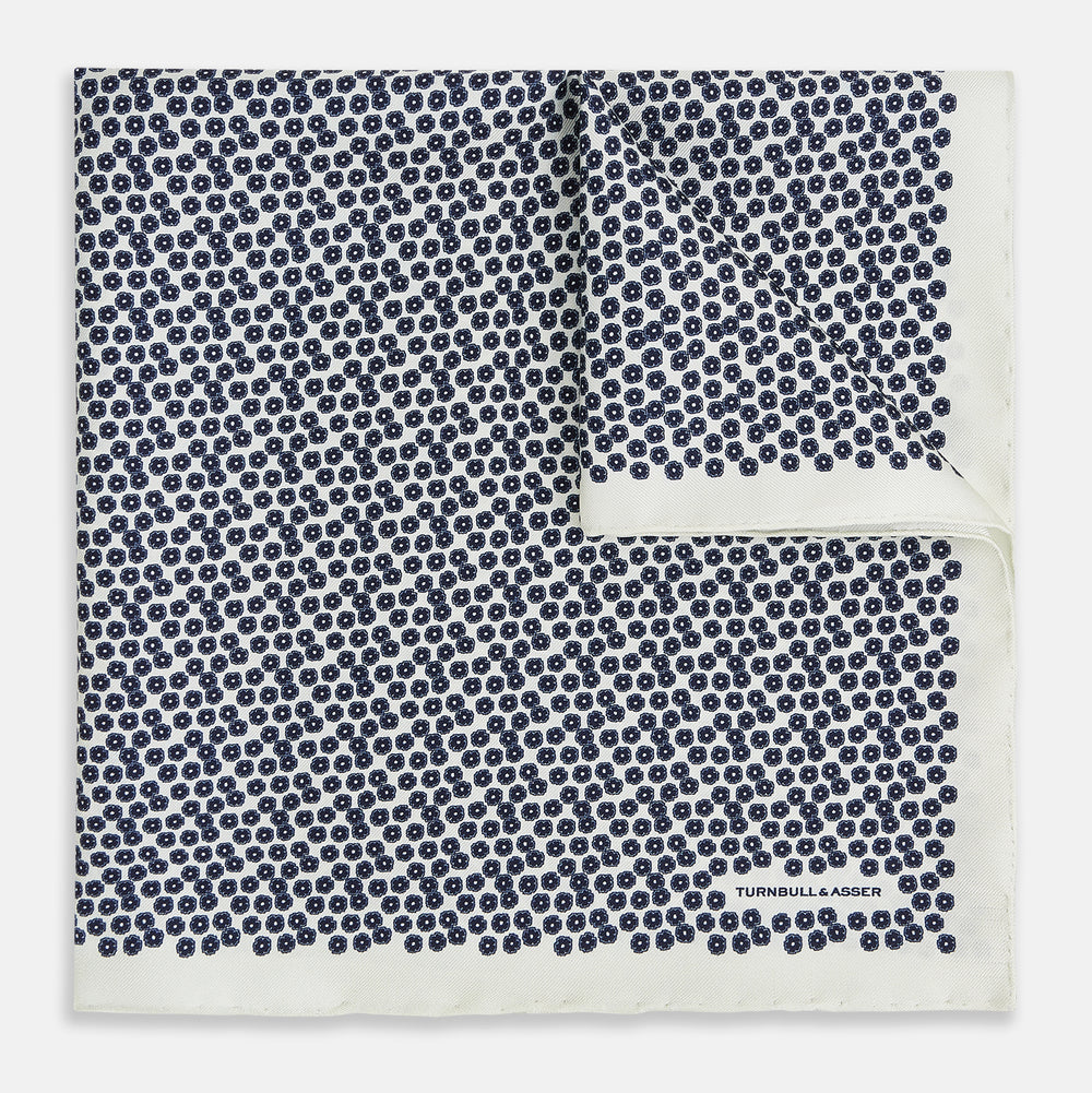 A refined double-sided design, the Floral White Pocket Square in Silk by Turnbull & Asser UK features a small blue floral pattern on white silk, neatly folded to display both its intricate front and bordered corner—adding subtle elegance to any ensemble.
