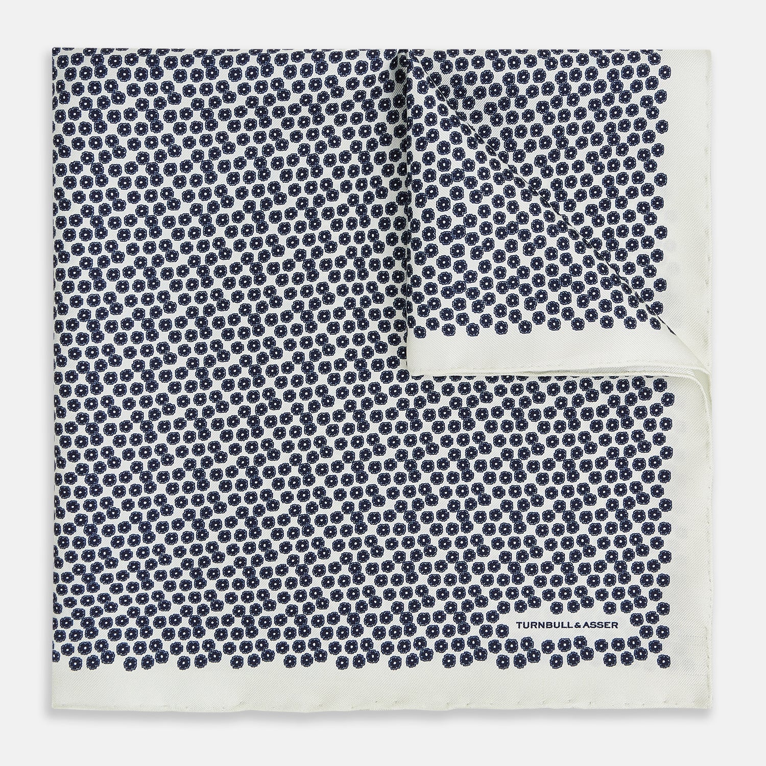 View 1 of product A refined double-sided design, the Floral White Pocket Square in Silk by Turnbull & Asser UK features a small blue floral pattern on white silk, neatly folded to display both its intricate front and bordered corner—adding subtle elegance to any ensemble.
