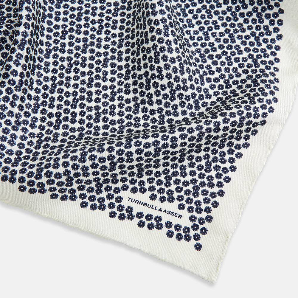 A refined double-sided design, the Floral White Pocket Square in Silk by Turnbull & Asser UK features a small blue floral pattern on white silk, neatly folded to display both its intricate front and bordered corner—adding subtle elegance to any ensemble.