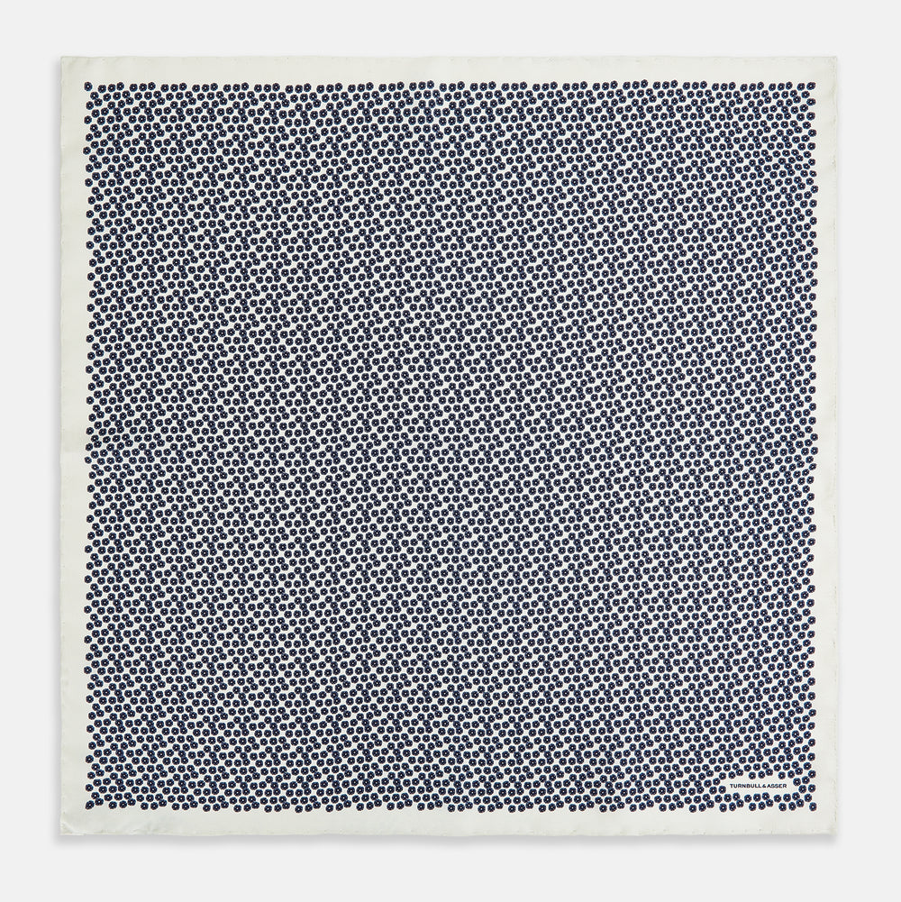 A refined double-sided design, the Floral White Pocket Square in Silk by Turnbull & Asser UK features a small blue floral pattern on white silk, neatly folded to display both its intricate front and bordered corner—adding subtle elegance to any ensemble.