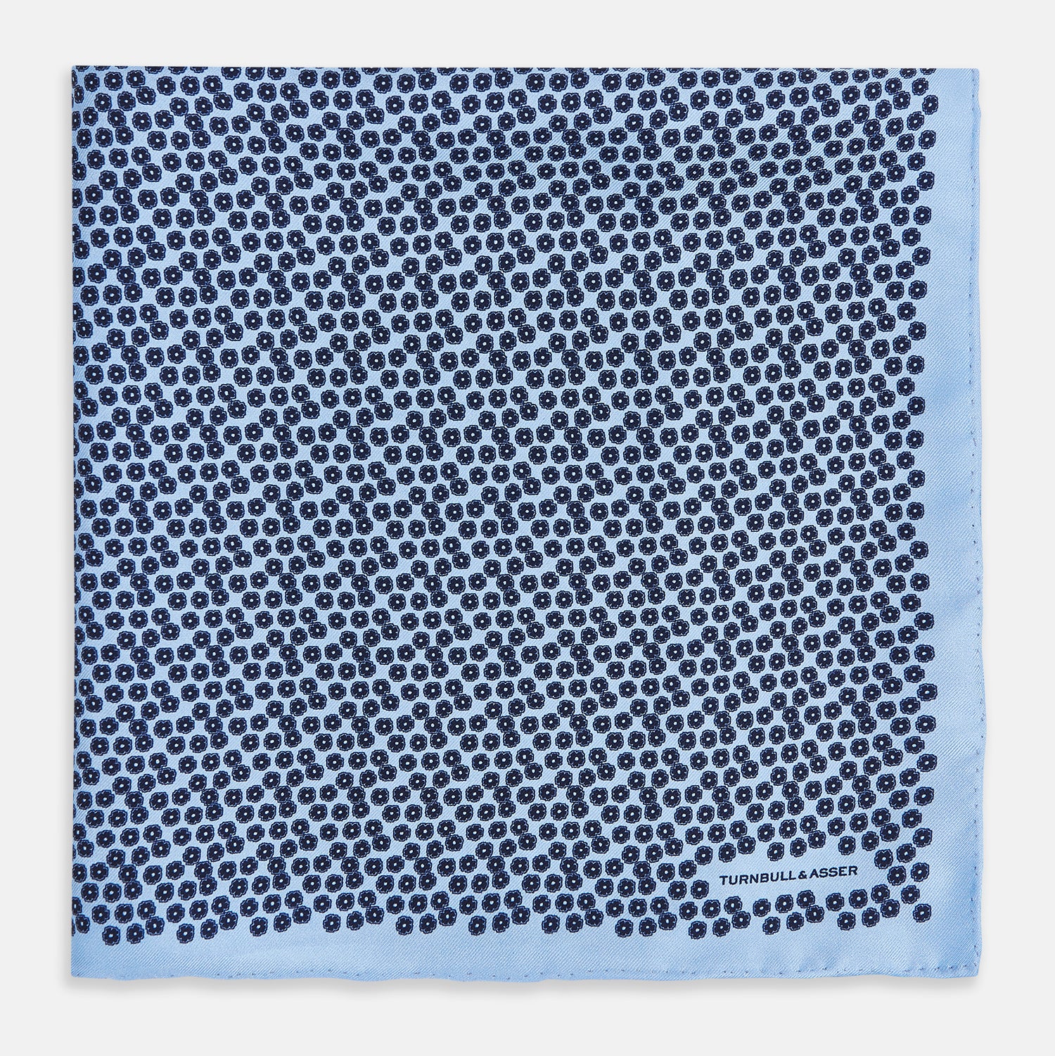 View 3 of product A light blue double-sided pocket square made of silk, featuring a dense pattern of small, dark blue floral motifs. One corner is folded over to reveal the Turnbull & Asser UK brand name printed in blue.