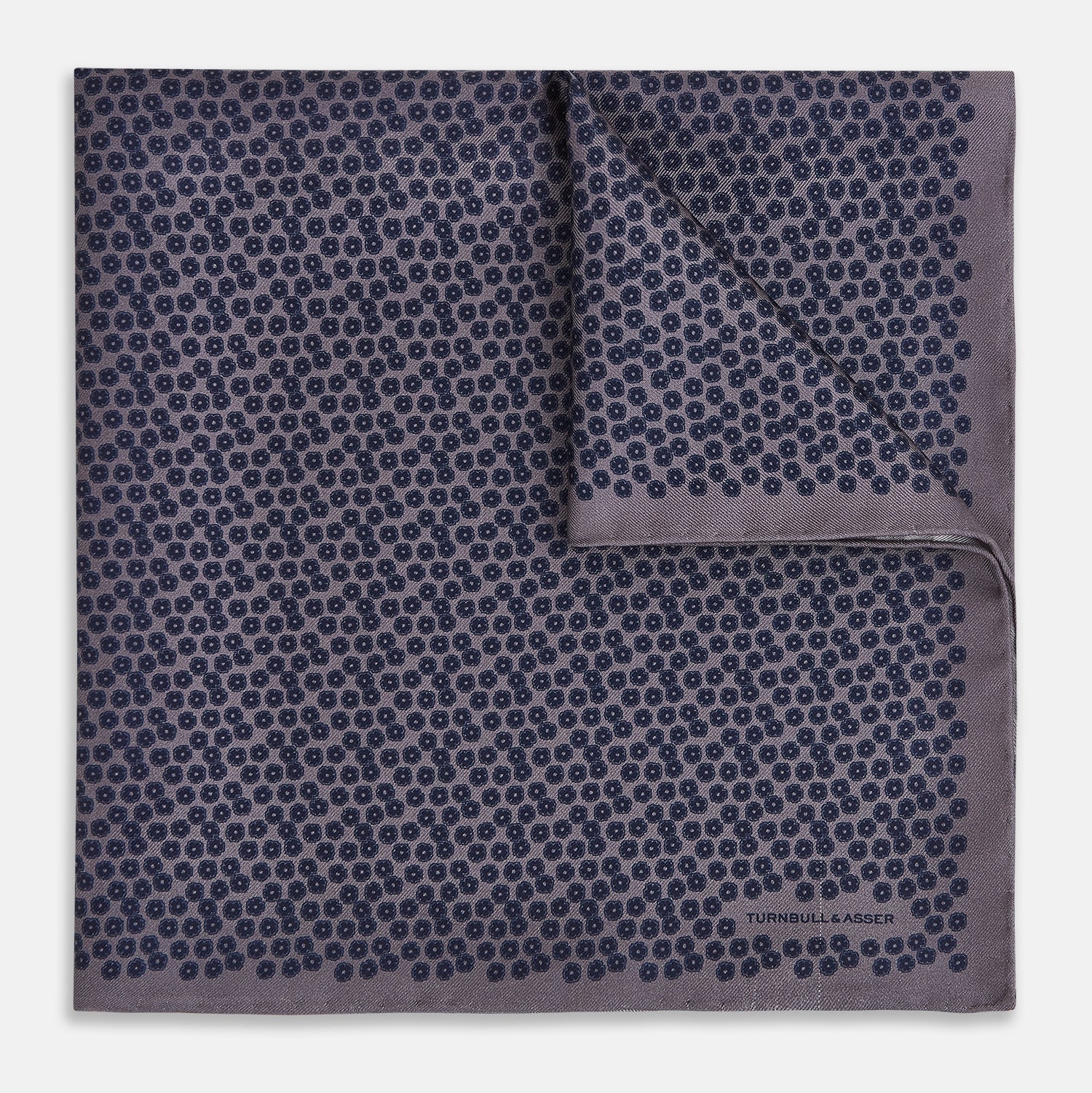 View 1 of product A folded Floral Purple Pocket Square in Silk by Turnbull & Asser UK, featuring a double-sided design with a pattern of small, dark blue circles and the brand’s logo printed in one corner.