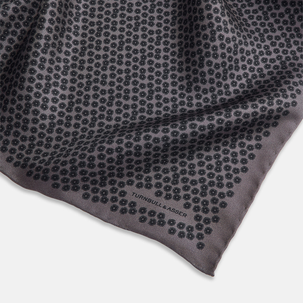 A folded Floral Purple Pocket Square in Silk by Turnbull & Asser UK, featuring a double-sided design with a pattern of small, dark blue circles and the brand’s logo printed in one corner.