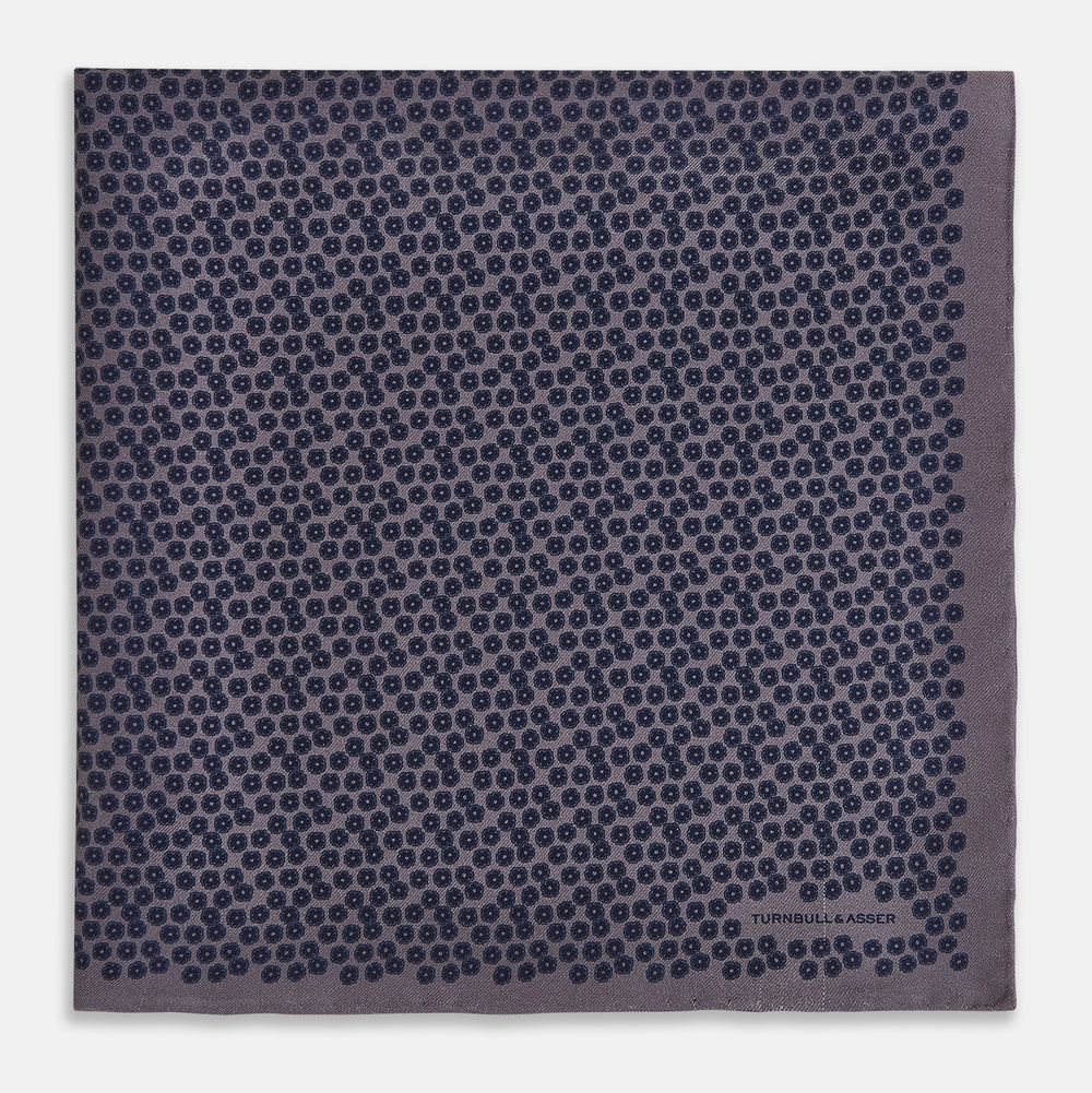 A folded Floral Purple Pocket Square in Silk by Turnbull & Asser UK, featuring a double-sided design with a pattern of small, dark blue circles and the brand’s logo printed in one corner.