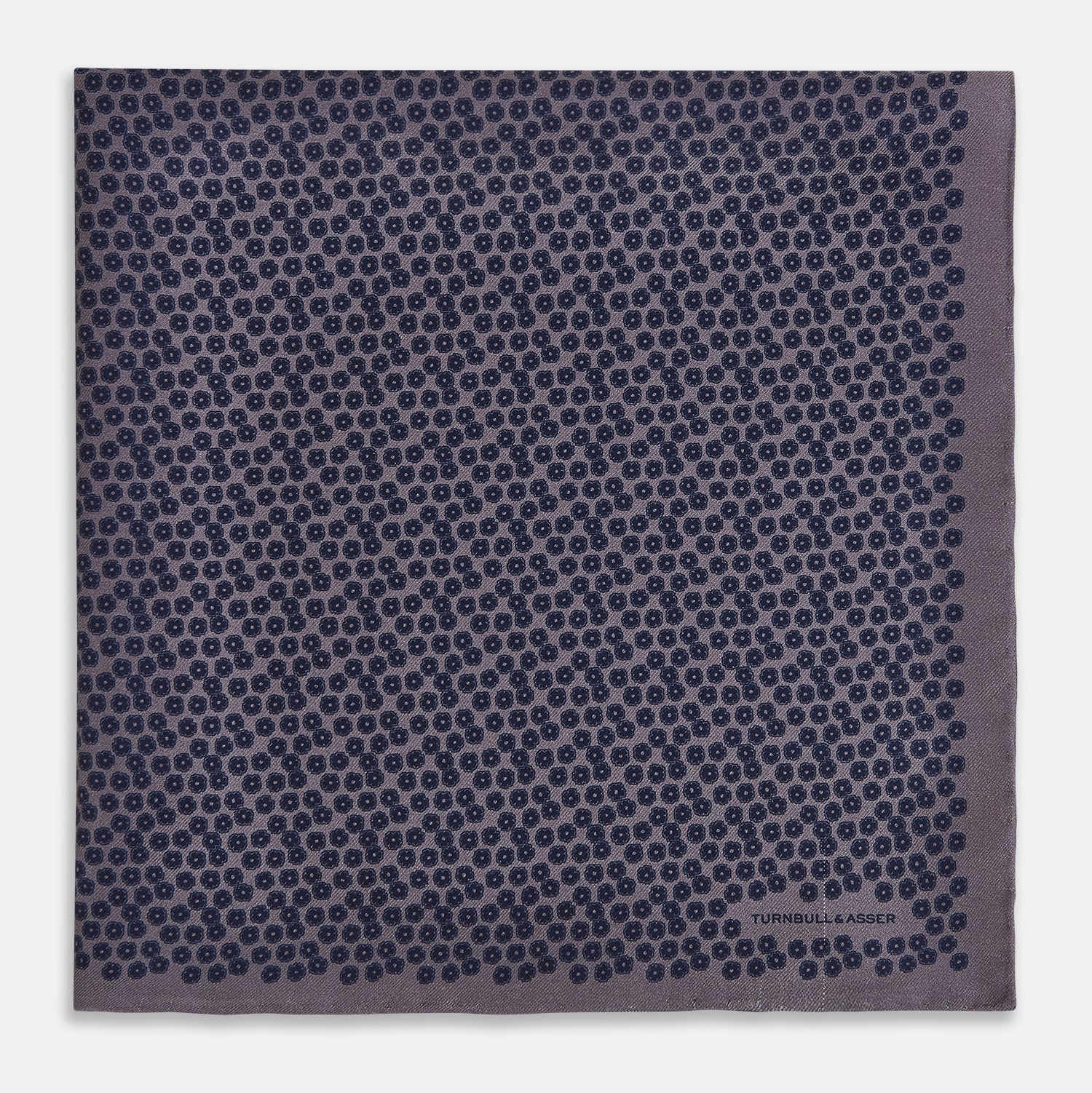 View 3 of product A folded Floral Purple Pocket Square in Silk by Turnbull & Asser UK, featuring a double-sided design with a pattern of small, dark blue circles and the brand’s logo printed in one corner.