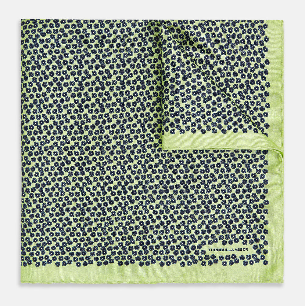 Introducing the Floral Green Pocket Square in Silk by Turnbull & Asser UK—a sophisticated accessory in light green silk, adorned with a delicate floral pattern and a folded corner. The pocket square features a refined double-sided design, with the Turnbull & Asser UK brand name elegantly printed on one corner.