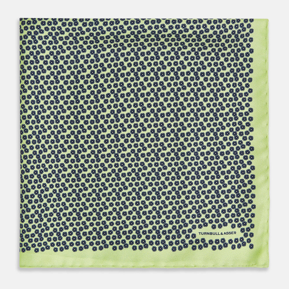 Introducing the Floral Green Pocket Square in Silk by Turnbull & Asser UK—a sophisticated accessory in light green silk, adorned with a delicate floral pattern and a folded corner. The pocket square features a refined double-sided design, with the Turnbull & Asser UK brand name elegantly printed on one corner.