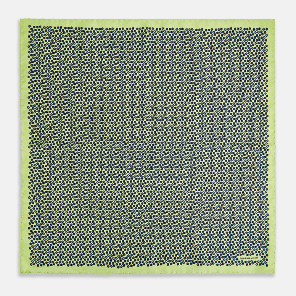 Introducing the Floral Green Pocket Square in Silk by Turnbull & Asser UK—a sophisticated accessory in light green silk, adorned with a delicate floral pattern and a folded corner. The pocket square features a refined double-sided design, with the Turnbull & Asser UK brand name elegantly printed on one corner.