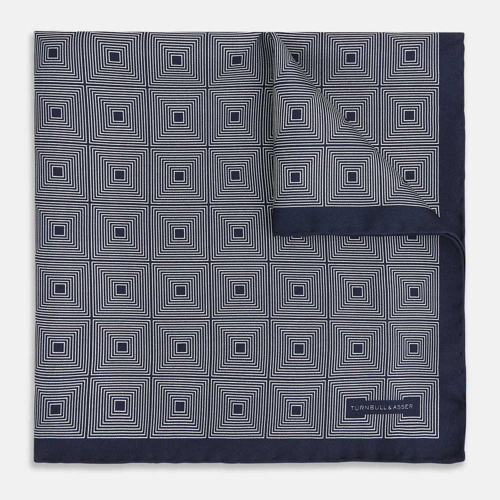 A Geometric Blue Pocket Square in Silk by Turnbull & Asser UK, featuring a navy blue and white geometric square tile design and a small label in the bottom right corner.