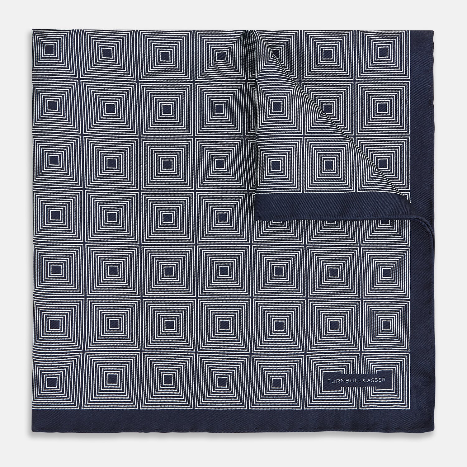 View 1 of product A Geometric Blue Pocket Square in Silk by Turnbull & Asser UK, featuring a navy blue and white geometric square tile design and a small label in the bottom right corner.