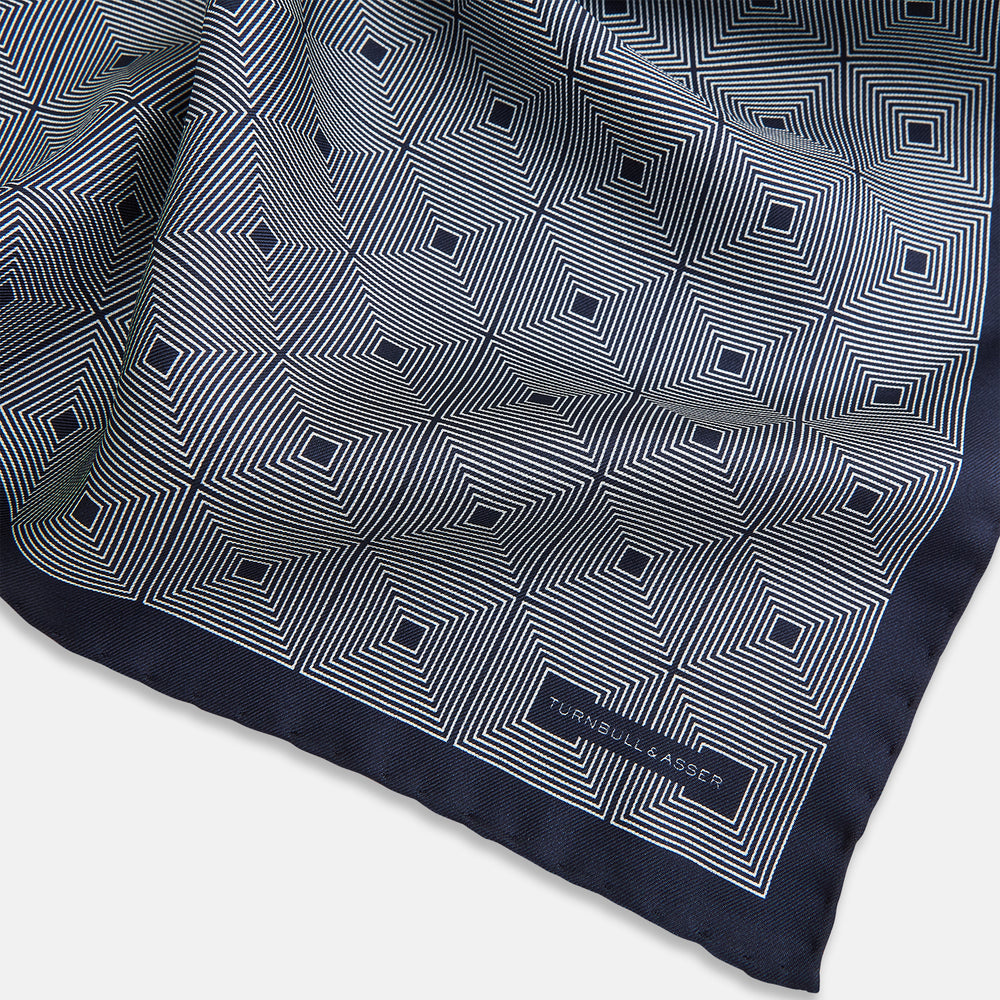 A Geometric Blue Pocket Square in Silk by Turnbull & Asser UK, featuring a navy blue and white geometric square tile design and a small label in the bottom right corner.