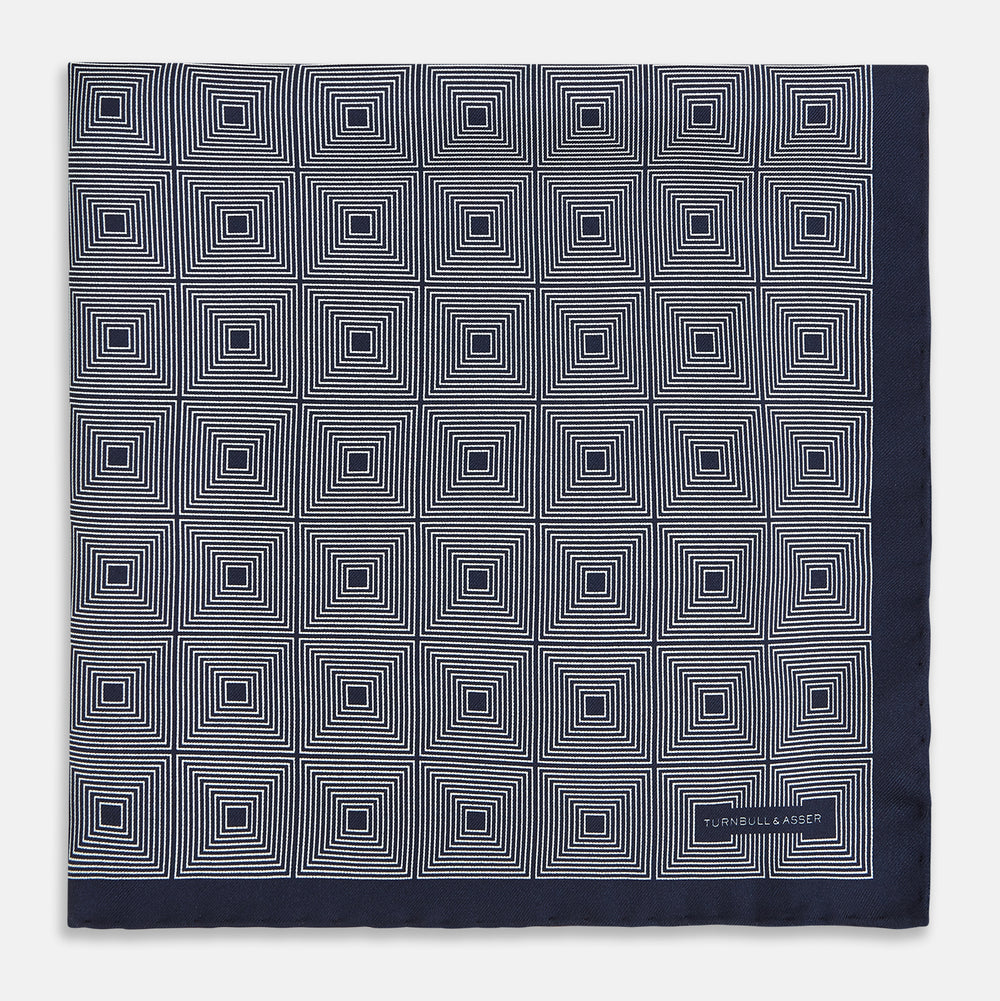 A Geometric Blue Pocket Square in Silk by Turnbull & Asser UK, featuring a navy blue and white geometric square tile design and a small label in the bottom right corner.