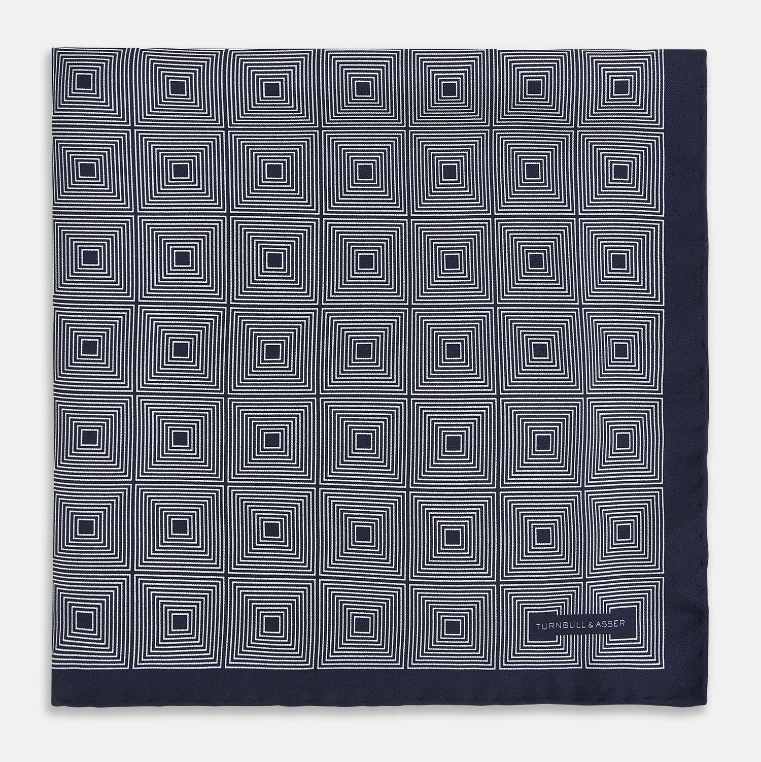 View 3 of product A Geometric Blue Pocket Square in Silk by Turnbull & Asser UK, featuring a navy blue and white geometric square tile design and a small label in the bottom right corner.
