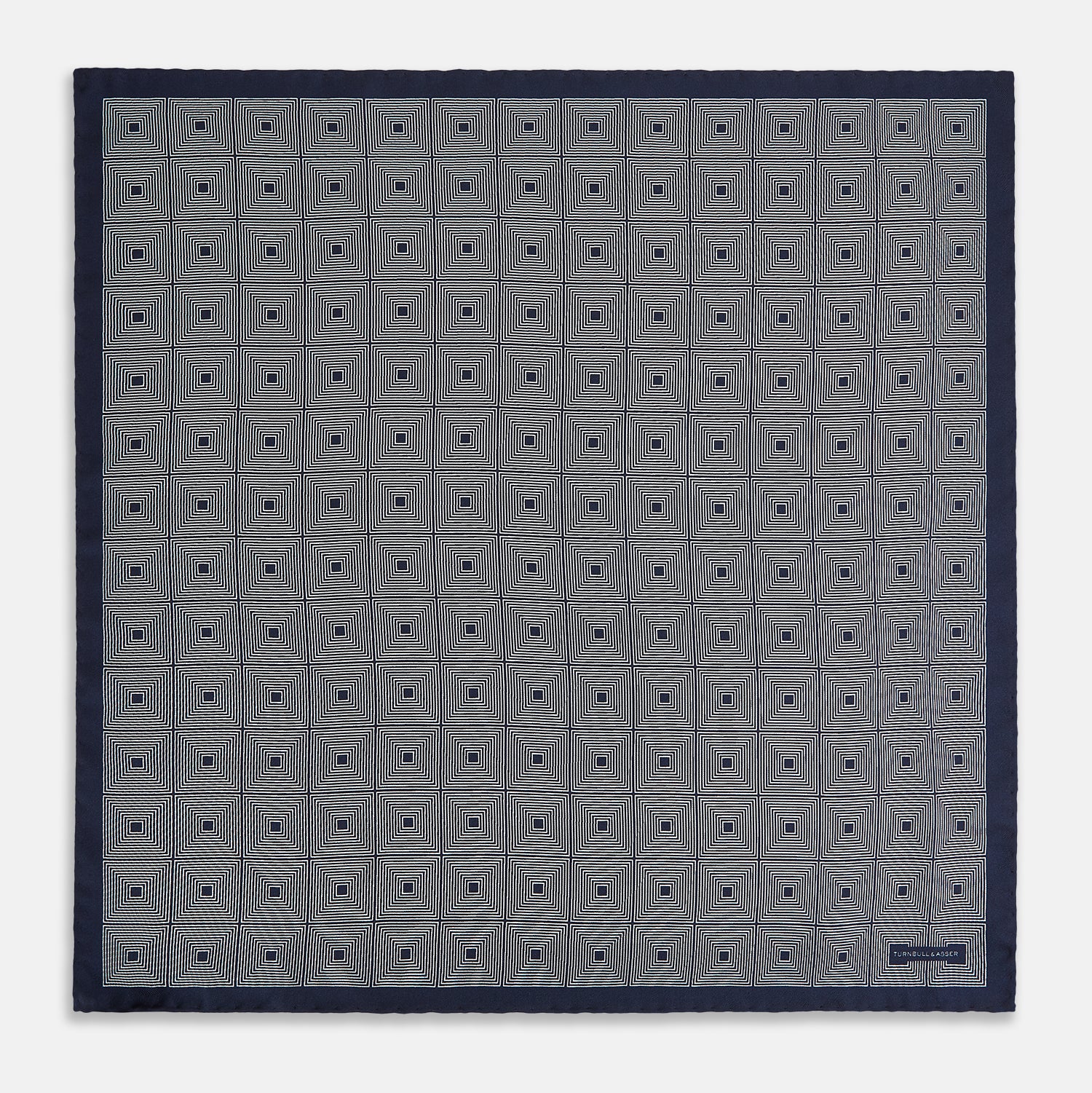 View 4 of product A Geometric Blue Pocket Square in Silk by Turnbull & Asser UK, featuring a navy blue and white geometric square tile design and a small label in the bottom right corner.