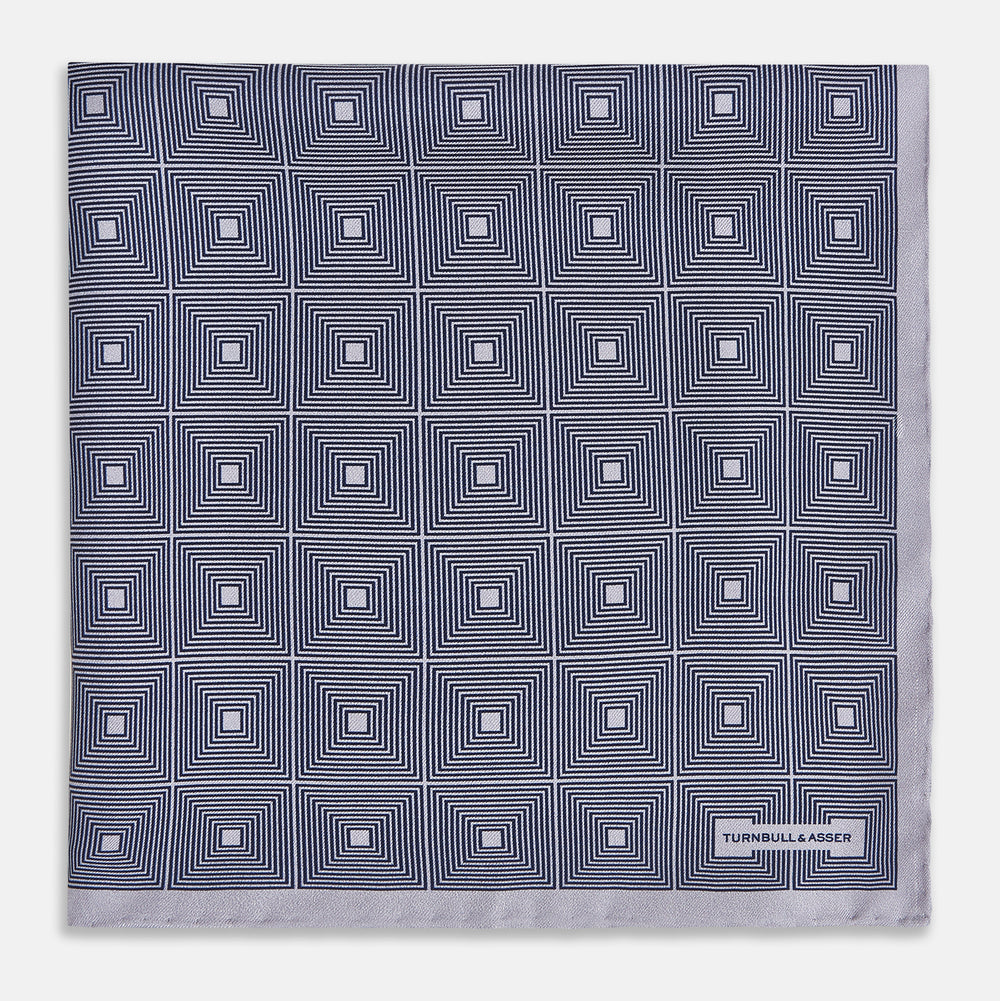 A folded, square Turnbull & Asser UK Geometric Grey Pocket Square in Silk featuring a geometric black and white concentric squares pattern accented with subtle navy lines, finished with a small Turnbull & Asser label in one corner.