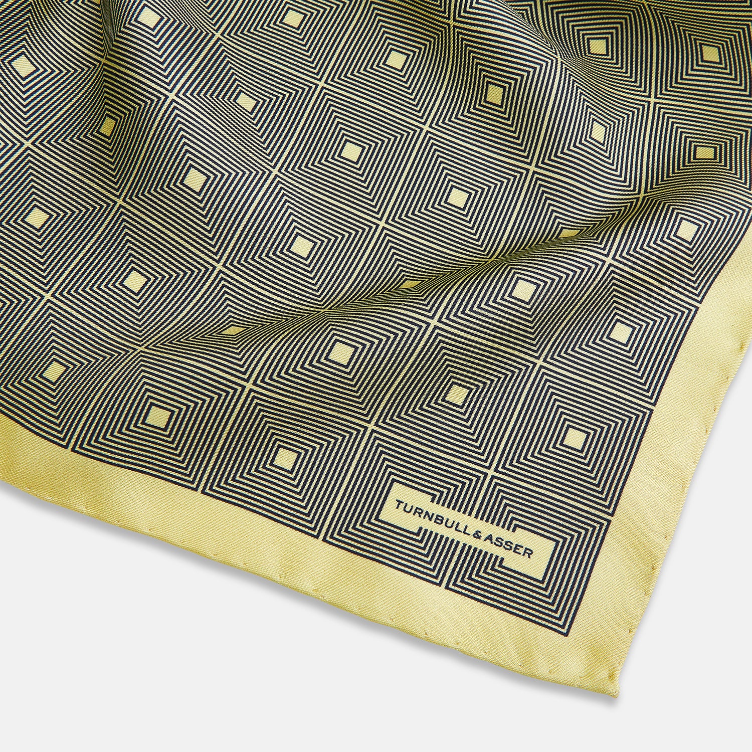 View 2 of product A checked yellow silk pocket square from Turnbull & Asser UK, featuring black and white concentric square designs with a yellow border. It is partially folded to highlight its double-sided pattern, and a small label reading TURNBULL & ASSER is visible in one corner.