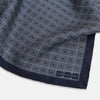 View 2 of product A Geometric Navy Pocket Square in Silk by Turnbull & Asser UK, showcasing a geometric pattern of small, overlapping concentric white squares and a stitched border. The pocket square is pictured with one corner folded over to display the Turnbull & Asser UK brand label.