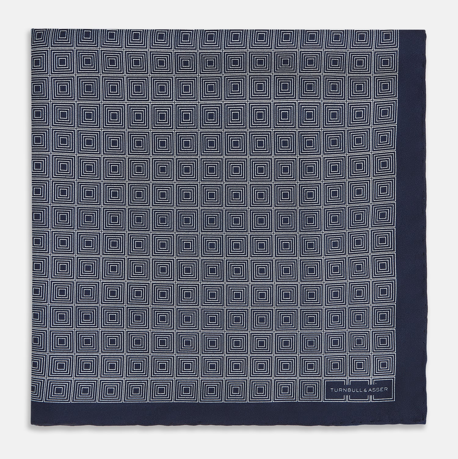 View 3 of product A Geometric Navy Pocket Square in Silk by Turnbull & Asser UK, showcasing a geometric pattern of small, overlapping concentric white squares and a stitched border. The pocket square is pictured with one corner folded over to display the Turnbull & Asser UK brand label.