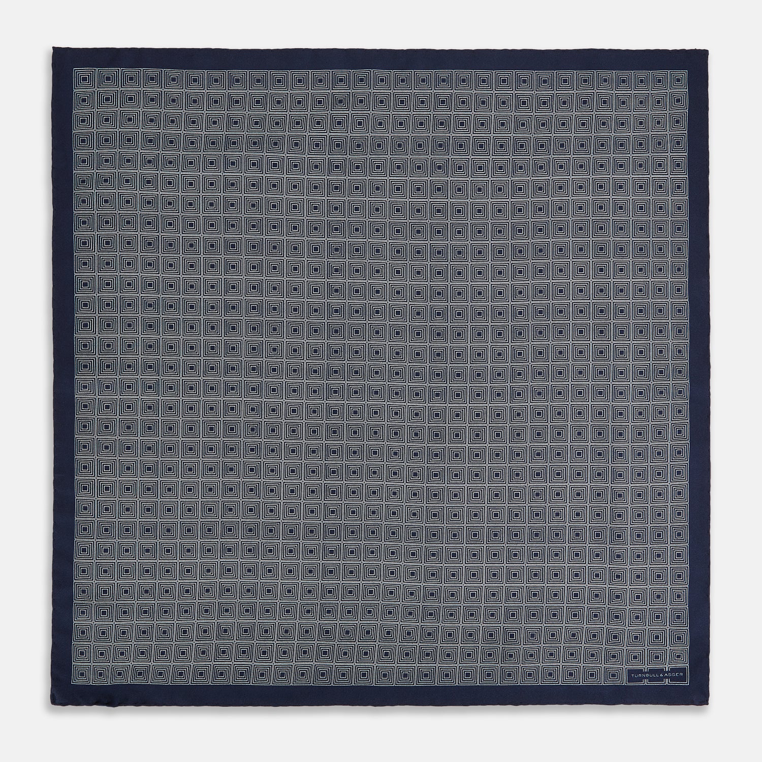 View 4 of product A Geometric Navy Pocket Square in Silk by Turnbull & Asser UK, showcasing a geometric pattern of small, overlapping concentric white squares and a stitched border. The pocket square is pictured with one corner folded over to display the Turnbull & Asser UK brand label.