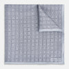 View 1 of product Geometric silver pocket square in silk by Turnbull & Asser UK, featuring a striking pattern of dark blue concentric squares. One corner of the fabric is folded to reveal the reverse side, with the brand name Turnbull & Asser UK printed elegantly in one corner.