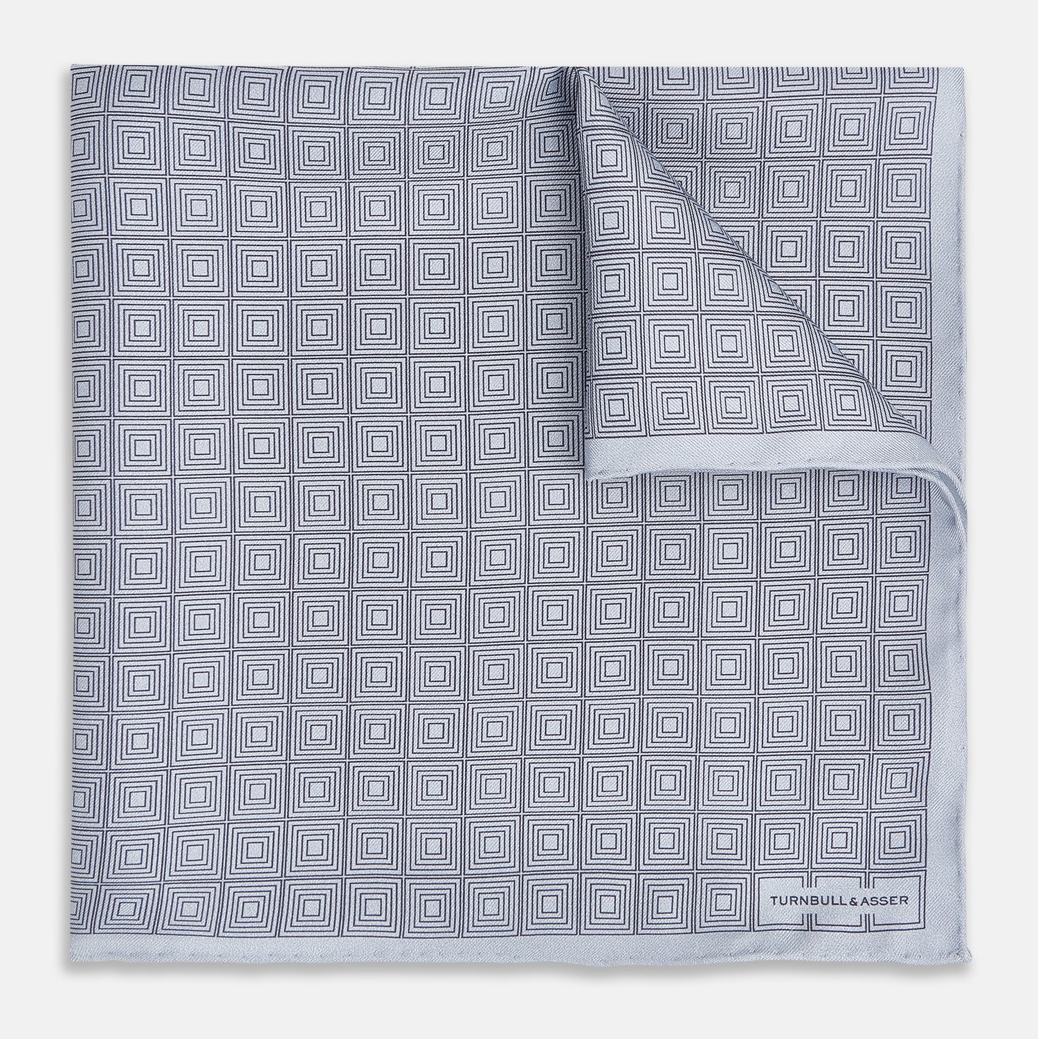 View 1 of product Geometric silver pocket square in silk by Turnbull & Asser UK, featuring a striking pattern of dark blue concentric squares. One corner of the fabric is folded to reveal the reverse side, with the brand name Turnbull & Asser UK printed elegantly in one corner.