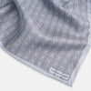 View 2 of product Geometric silver pocket square in silk by Turnbull & Asser UK, featuring a striking pattern of dark blue concentric squares. One corner of the fabric is folded to reveal the reverse side, with the brand name Turnbull & Asser UK printed elegantly in one corner.