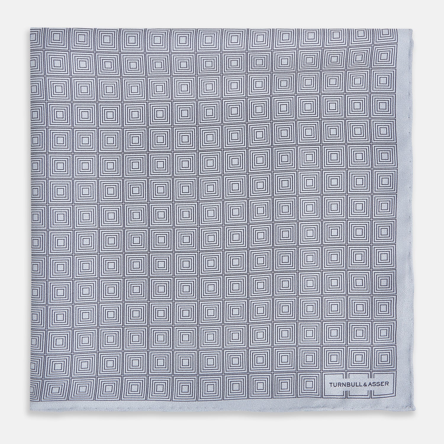 View 3 of product Geometric silver pocket square in silk by Turnbull & Asser UK, featuring a striking pattern of dark blue concentric squares. One corner of the fabric is folded to reveal the reverse side, with the brand name Turnbull & Asser UK printed elegantly in one corner.