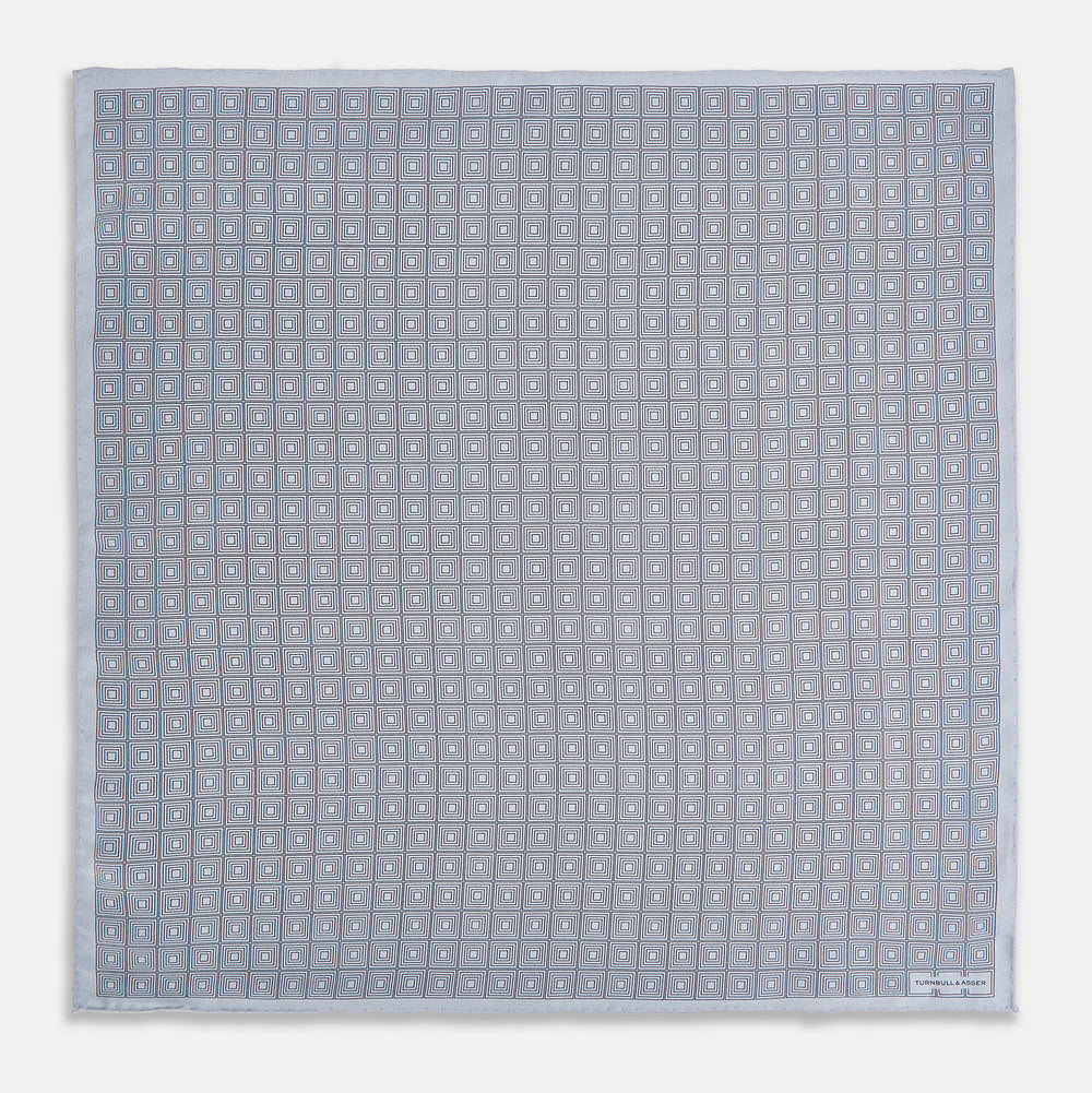 Geometric silver pocket square in silk by Turnbull & Asser UK, featuring a striking pattern of dark blue concentric squares. One corner of the fabric is folded to reveal the reverse side, with the brand name Turnbull & Asser UK printed elegantly in one corner.
