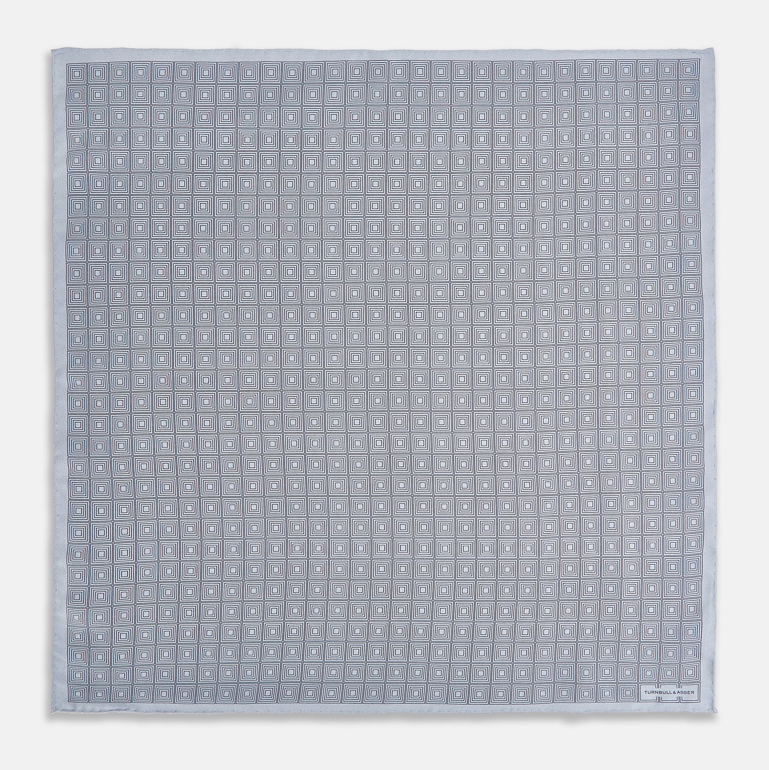 View 4 of product Geometric silver pocket square in silk by Turnbull & Asser UK, featuring a striking pattern of dark blue concentric squares. One corner of the fabric is folded to reveal the reverse side, with the brand name Turnbull & Asser UK printed elegantly in one corner.